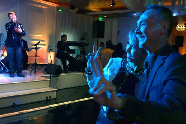 Duy Nguyen-Amigo, far left, dedicates a song to his parents, as he performs on stage. His parents, Thuy, left, and Hung Nguyen, hug, pose for photos, and dance to his performance. They are at their banquet hall, Mon Amour, in the city of Anaheim. (Photo by Karen Tapia, Contributing Photographer)