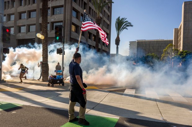 A defiant protester waves the American flag as federal police fire tear gas at protesters outside the Federal Building in Santa Ana on Monday, June 9, 2025. (Photo by Leonard Ortiz, Orange County Register/SCNG)