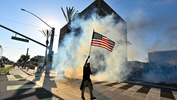 A protester raises the U.S. flag after police use tear gas and flash-bangs at the Federal Building in Santa Ana, CA, on Monday, June 9, 2025. About 200 anti-ICE protesters spent the afternoon carrying signs as they chanted and yelled at police. (Photo by Jeff Gritchen, Orange County Register/SCNG)