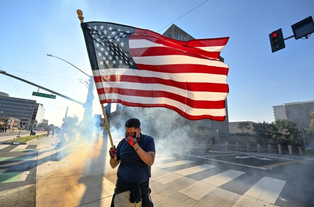 A protester raises the U.S. flag after police use tear gas and flash-bangs at the Federal Building in Santa Ana, CA, on Monday, June 9, 2025. About 200 anti-ICE protesters spent the afternoon carrying signs as they chanted and yelled at police. (Photo by Jeff Gritchen, Orange County Register/SCNG)