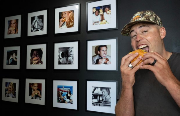 Jordan Smalls, owner of the new Smalls Smash Club in San Clemente, mimics the restaurant's photo wall of hamburger-eating celebrities on Wednesday, July 16, 2025. Smalls is also a pro snowboarder. (Photo by Mindy Schauer, Orange County Register/SCNG)