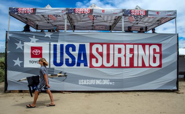 A surfer walks past a banner at the USA Surfing Championships held at Lower Trestles at San Onofre State Beach south of San Clemente on Friday, June 21, 2019. (Photo by Mark Rightmire, Orange County Register/SCNG)